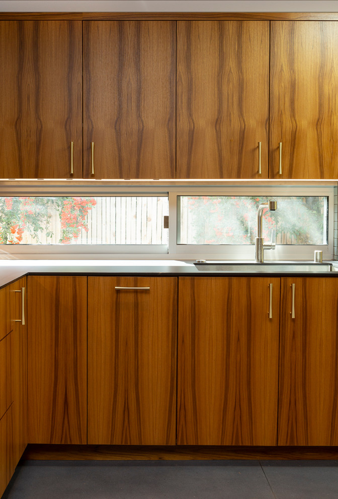 Inspiration for a mid-sized midcentury u-shaped open plan kitchen in Sacramento with a drop-in sink, flat-panel cabinets, medium wood cabinets, beige splashback, ceramic splashback, stainless steel appliances, concrete floors, with island, grey floor and black benchtop.