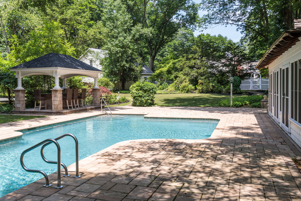 Photo of a large traditional backyard custom-shaped pool in Boston with a pool house and natural stone pavers.