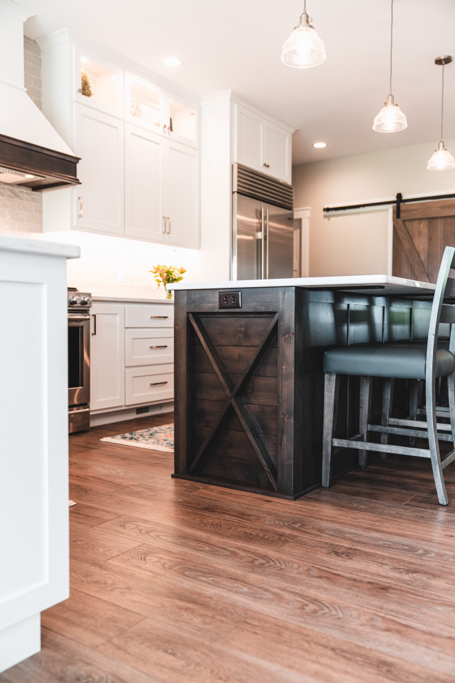 Kitchen pantry - large transitional l-shaped vinyl floor and brown floor kitchen pantry idea with an undermount sink, shaker cabinets, white cabinets, quartz countertops, gray backsplash, subway tile backsplash, stainless steel appliances, an island and white countertops