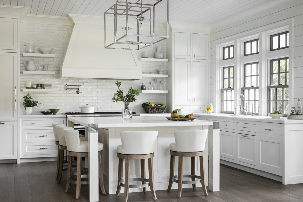 Example of a beach style l-shaped dark wood floor and brown floor kitchen design in New York with an undermount sink, recessed-panel cabinets, white cabinets, white backsplash, subway tile backsplash, an island and white countertops