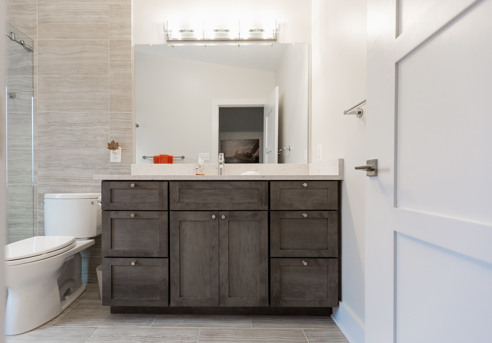Photo of a mid-sized modern 3/4 bathroom in DC Metro with shaker cabinets, distressed cabinets, a two-piece toilet, beige tile, stone tile, white walls, porcelain floors, an undermount sink, engineered quartz benchtops, beige floor and white benchtops.