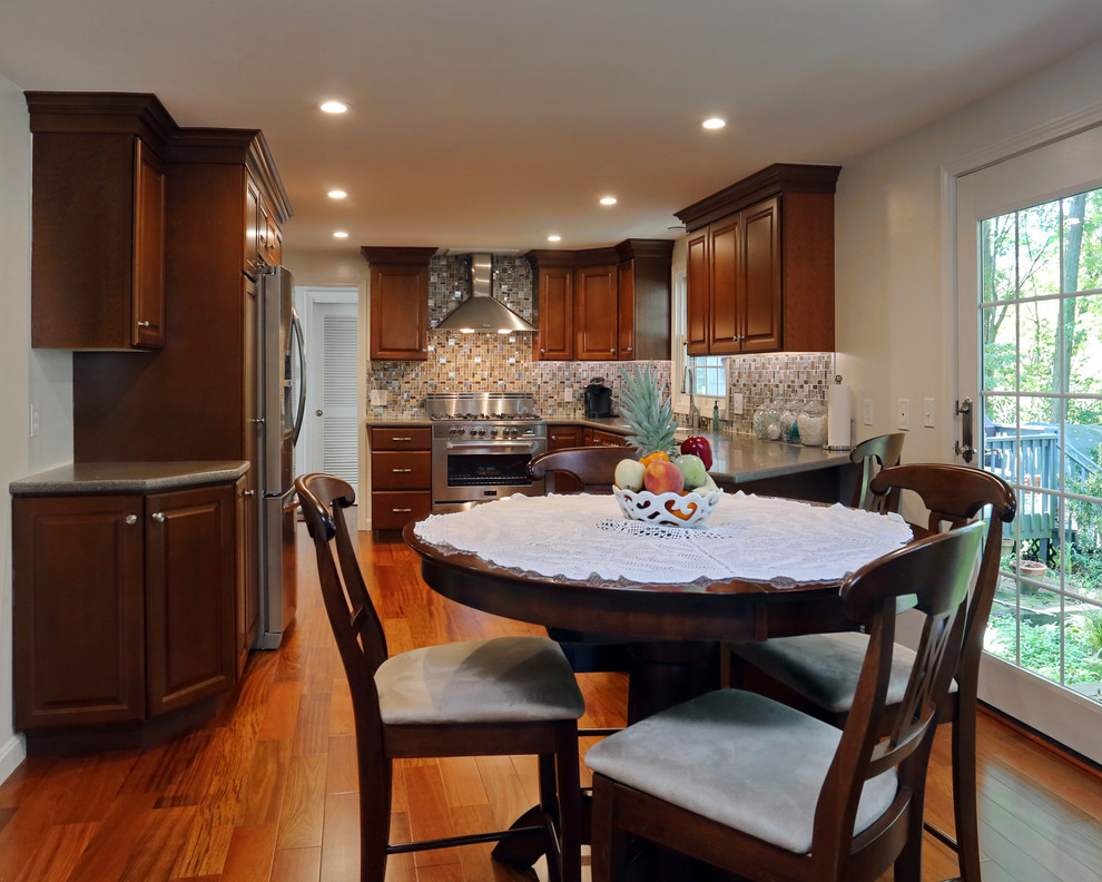 Example of a mid-sized transitional u-shaped medium tone wood floor eat-in kitchen design in Boston with an integrated sink, dark wood cabinets, solid surface countertops, blue backsplash, glass tile backsplash and stainless steel appliances