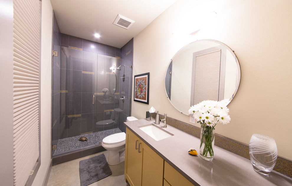 Mid-sized contemporary kids bathroom in Austin with laminate benchtops, a two-piece toilet, beige walls, concrete floors, shaker cabinets, yellow cabinets, an alcove shower, gray tile, porcelain tile and an undermount sink.