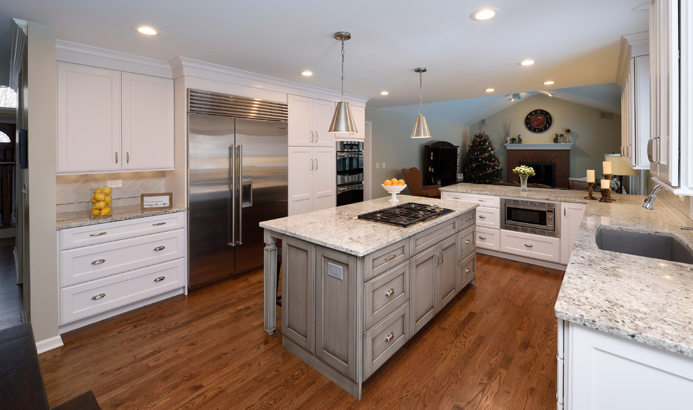 Large transitional l-shaped medium tone wood floor open concept kitchen photo in Chicago with an undermount sink, recessed-panel cabinets, white cabinets, granite countertops, gray backsplash, ceramic backsplash, stainless steel appliances and an island
