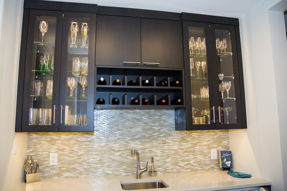This is an example of a small contemporary single-wall wet bar in DC Metro with an undermount sink, flat-panel cabinets, dark wood cabinets, quartz benchtops, multi-coloured splashback, glass sheet splashback, porcelain floors, grey floor and white benchtop.