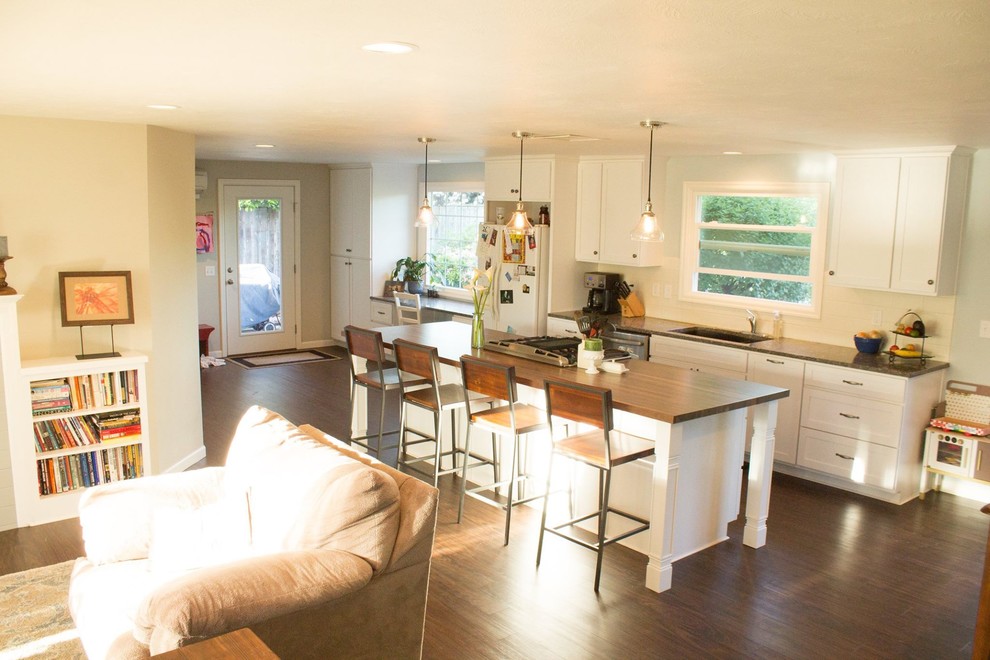 Inspiration for a mid-sized transitional galley dark wood floor and brown floor open concept kitchen remodel with an undermount sink, shaker cabinets, white cabinets, wood countertops, white backsplash, porcelain backsplash, white appliances and an island