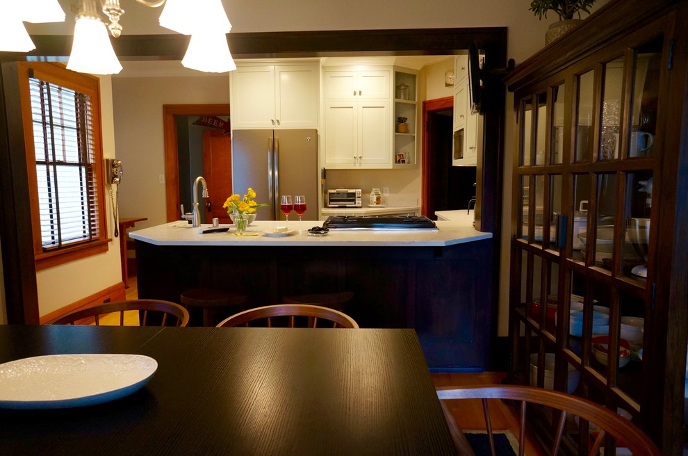 This is an example of a small arts and crafts galley eat-in kitchen in Minneapolis with a farmhouse sink, shaker cabinets, grey cabinets, quartz benchtops, stone slab splashback, stainless steel appliances, light hardwood floors and a peninsula.