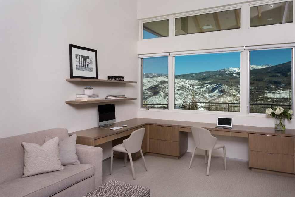 This is an example of a mid-sized modern study room in Denver with white walls, carpet, a two-sided fireplace, a plaster fireplace surround, a built-in desk and beige floor.