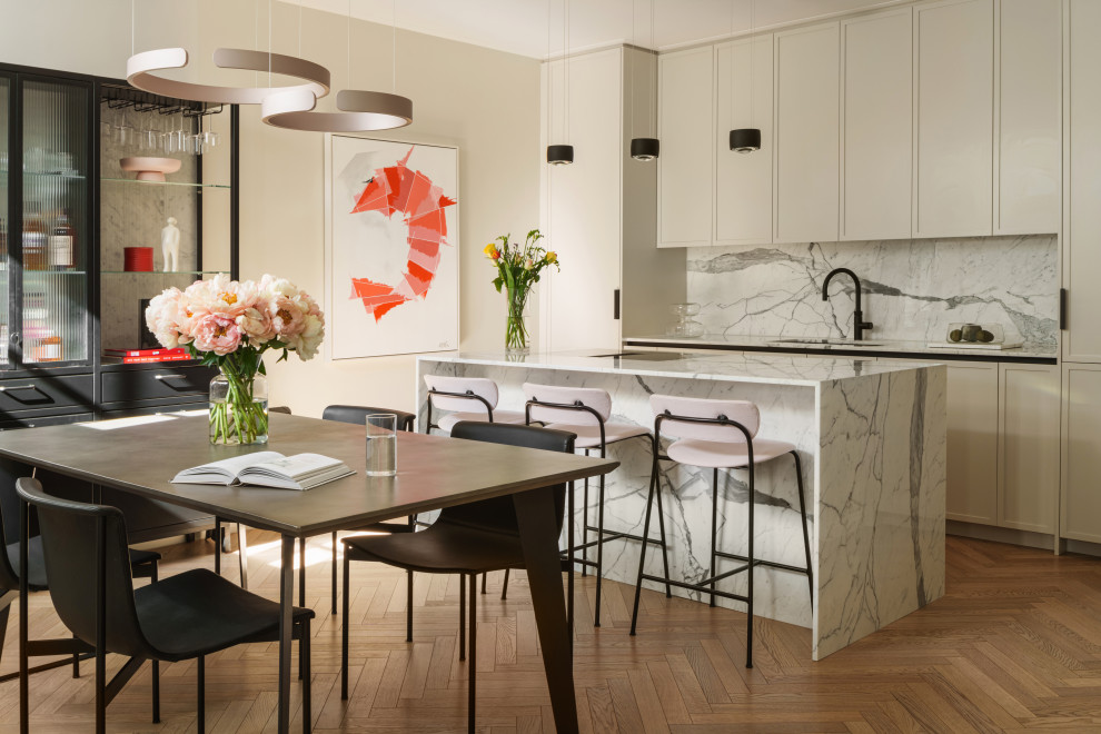 Inspiration for a contemporary galley kitchen/diner in London with a submerged sink, shaker cabinets, white cabinets, white splashback, stone slab splashback, integrated appliances, medium hardwood flooring, an island, brown floors and white worktops.
