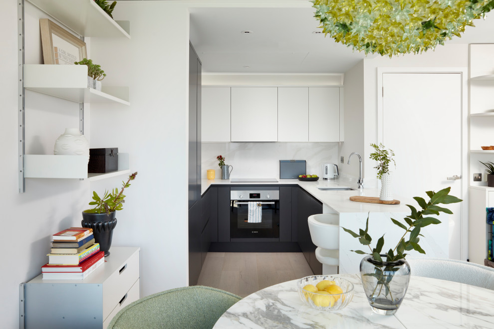 This is an example of a small contemporary u-shaped eat-in kitchen in London with a drop-in sink, flat-panel cabinets, white cabinets, quartzite benchtops, red splashback, ceramic splashback, stainless steel appliances, light hardwood floors and white benchtop.
