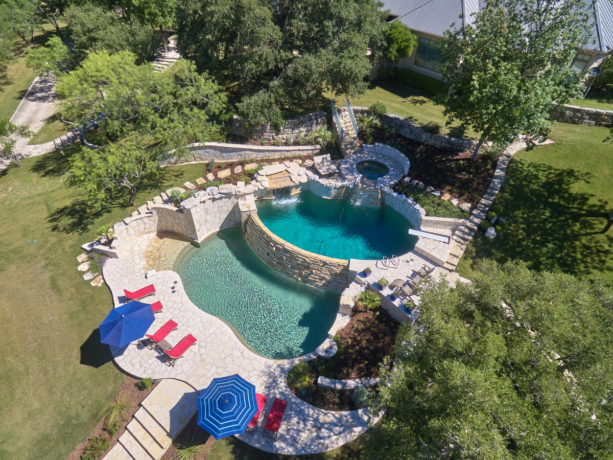Large island style backyard custom-shaped and stone infinity hot tub photo in Austin