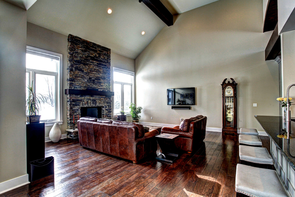 This is an example of a large arts and crafts open concept family room in Grand Rapids with brown walls, a standard fireplace, a stone fireplace surround, a wall-mounted tv and medium hardwood floors.