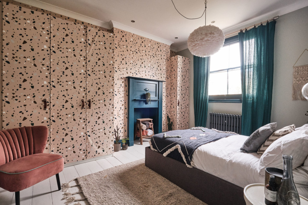 Photo of a mid-sized eclectic guest bedroom in London with blue walls, painted wood floors, a standard fireplace, a wood fireplace surround, white floor, vaulted and wallpaper.