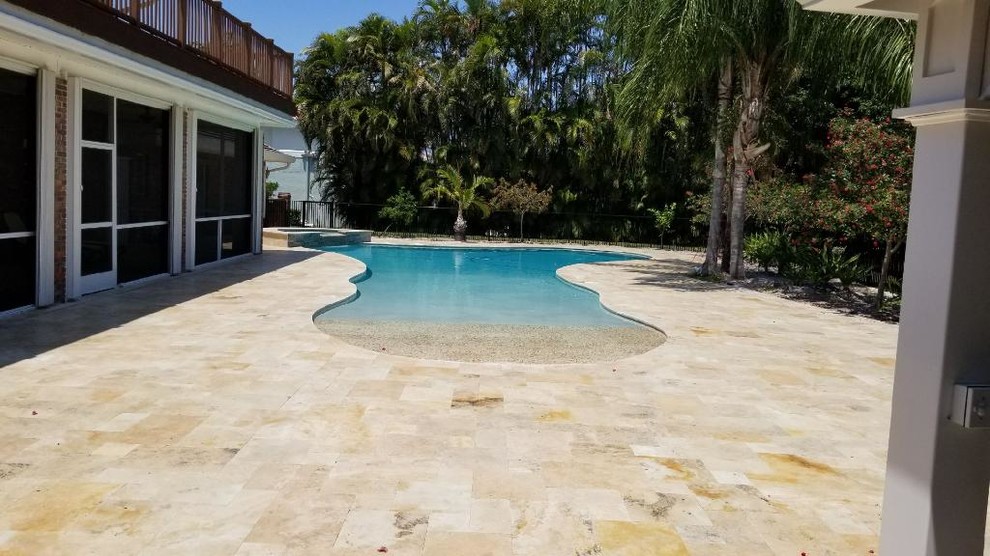 Photo of a mid-sized beach style backyard custom-shaped natural pool in Miami with natural stone pavers.