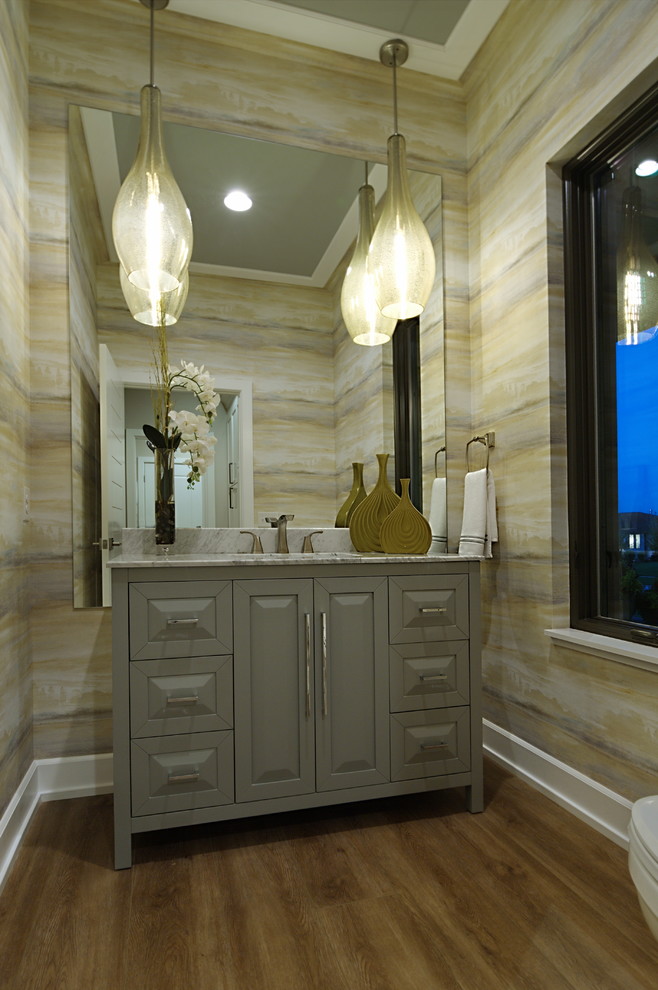 Photo of a large midcentury bathroom in Omaha with furniture-like cabinets, grey cabinets, a two-piece toilet, beige tile, yellow walls, vinyl floors, an undermount sink, marble benchtops, beige floor and beige benchtops.