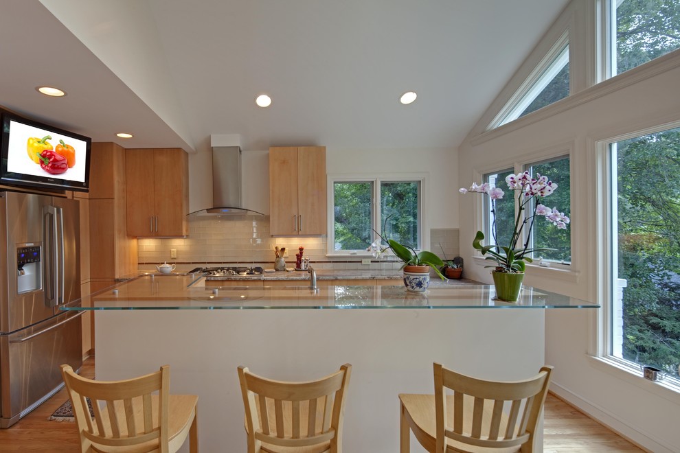 Photo of a contemporary kitchen in DC Metro with stainless steel appliances, glass benchtops, flat-panel cabinets, medium wood cabinets, white splashback and subway tile splashback.