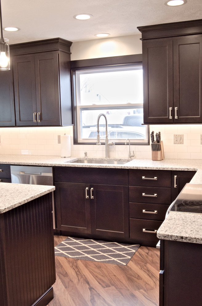 Example of a l-shaped kitchen design with a single-bowl sink, shaker cabinets, dark wood cabinets, granite countertops, white backsplash, stainless steel appliances and an island
