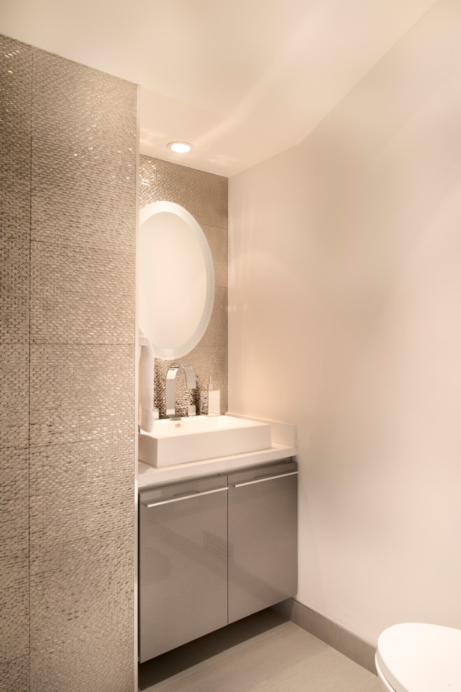 This is an example of a contemporary powder room in Santa Barbara with flat-panel cabinets, grey cabinets, gray tile, mosaic tile, a vessel sink and white benchtops.