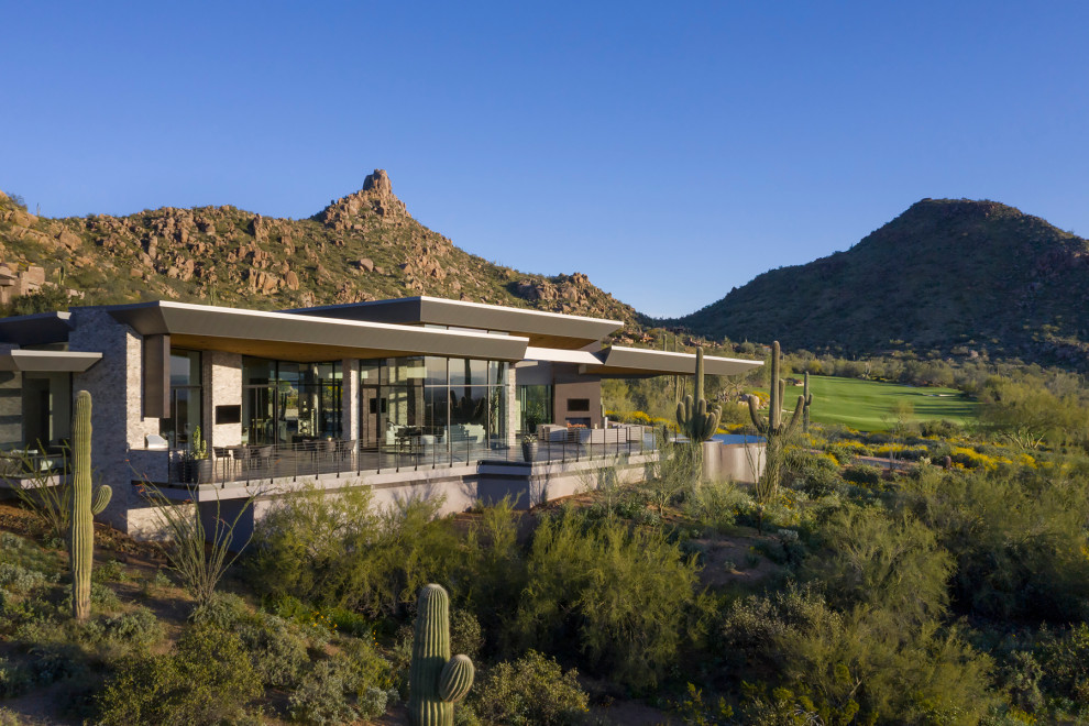This is an example of an expansive modern house exterior in Phoenix with stone veneer, a butterfly roof and a metal roof.
