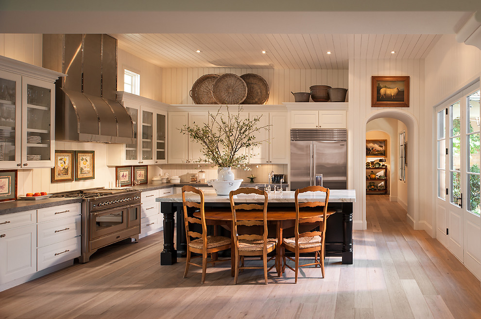 This is an example of a traditional l-shaped kitchen in Phoenix with raised-panel cabinets, white cabinets, stainless steel appliances, light hardwood floors and with island.