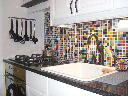 This is an example of a small eclectic single-wall separate kitchen in New York with a drop-in sink, recessed-panel cabinets, white cabinets, granite benchtops, multi-coloured splashback, glass tile splashback, black appliances and no island.