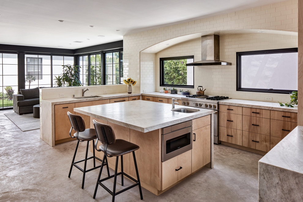 Design ideas for a mid-sized contemporary u-shaped open plan kitchen in Los Angeles with an undermount sink, flat-panel cabinets, light wood cabinets, quartzite benchtops, beige splashback, ceramic splashback, stainless steel appliances, concrete floors, with island, grey floor and beige benchtop.