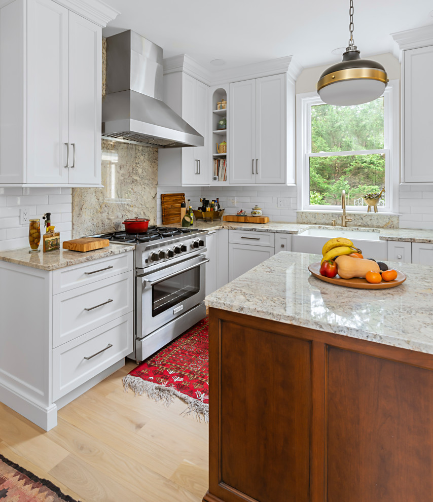 This is an example of a medium sized classic l-shaped enclosed kitchen in Philadelphia with a belfast sink, recessed-panel cabinets, granite worktops, white splashback, ceramic splashback, stainless steel appliances, light hardwood flooring, an island, beige floors and multicoloured worktops.