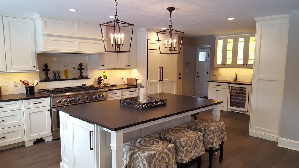Open concept kitchen - large transitional l-shaped dark wood floor and brown floor open concept kitchen idea in Detroit with a farmhouse sink, recessed-panel cabinets, white cabinets, granite countertops, white backsplash, subway tile backsplash, an island and stainless steel appliances