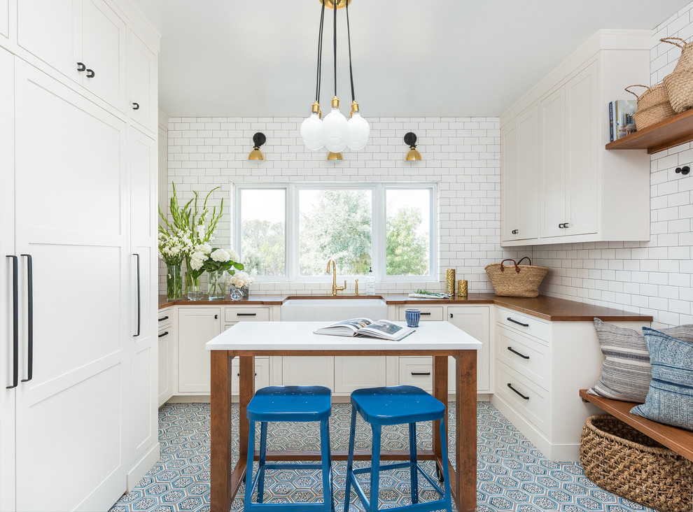 Inspiration for a transitional u-shaped laundry room in Albuquerque with a farmhouse sink, white cabinets, wood benchtops, white walls, terra-cotta floors, a concealed washer and dryer, blue floor and shaker cabinets.