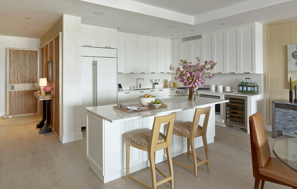 Design ideas for a beach style l-shaped eat-in kitchen in New York with an undermount sink, shaker cabinets, white cabinets, panelled appliances, light hardwood floors, with island and beige floor.