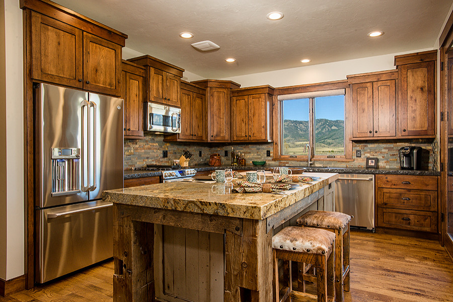 This is an example of a mid-sized country l-shaped kitchen in Other with a farmhouse sink, shaker cabinets, brown cabinets, granite benchtops, stainless steel appliances, medium hardwood floors, with island and brown floor.