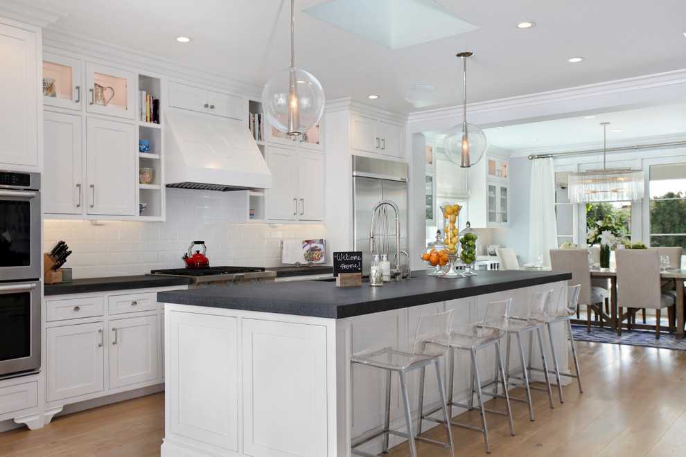 Transitional galley medium tone wood floor kitchen photo in Orange County with an undermount sink, shaker cabinets, white cabinets, white backsplash, subway tile backsplash, stainless steel appliances and an island