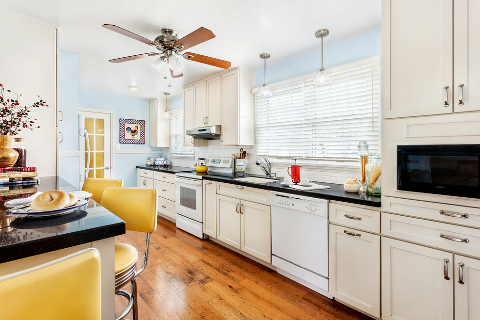 Transitional galley eat-in kitchen photo with an undermount sink, shaker cabinets, white cabinets, solid surface countertops, white backsplash, subway tile backsplash and white appliances