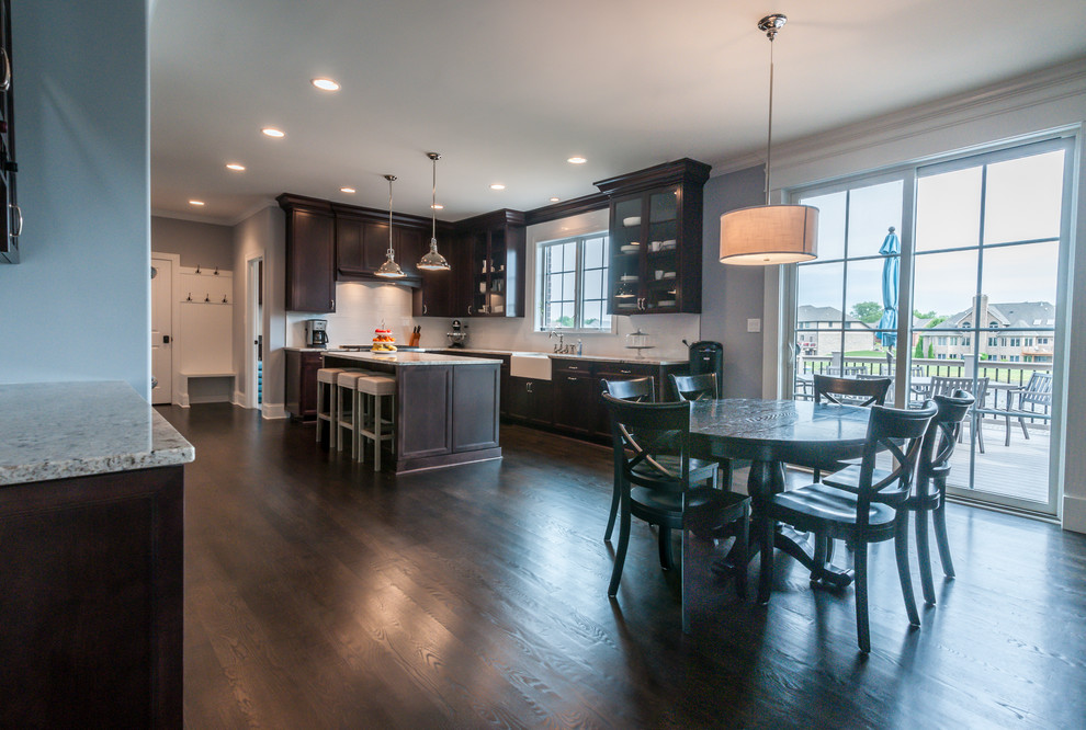 Large traditional u-shaped eat-in kitchen in Chicago with flat-panel cabinets, a farmhouse sink, dark wood cabinets, granite benchtops, white splashback, dark hardwood floors, with island, brown floor and multi-coloured benchtop.