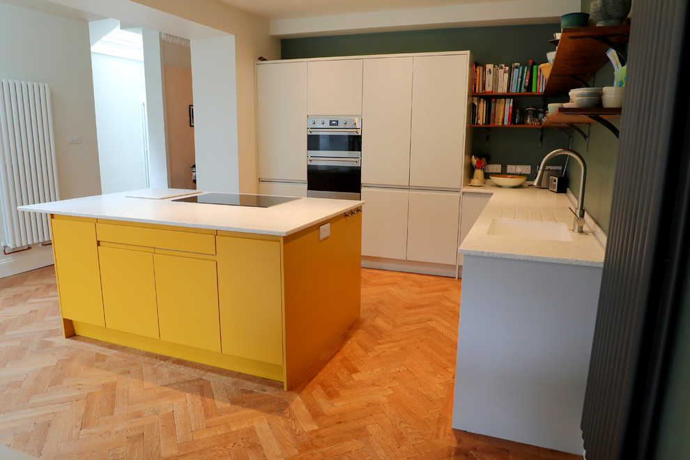 Photo of a mid-sized contemporary l-shaped open plan kitchen in Other with an integrated sink, flat-panel cabinets, yellow cabinets, solid surface benchtops, stainless steel appliances, with island and white benchtop.