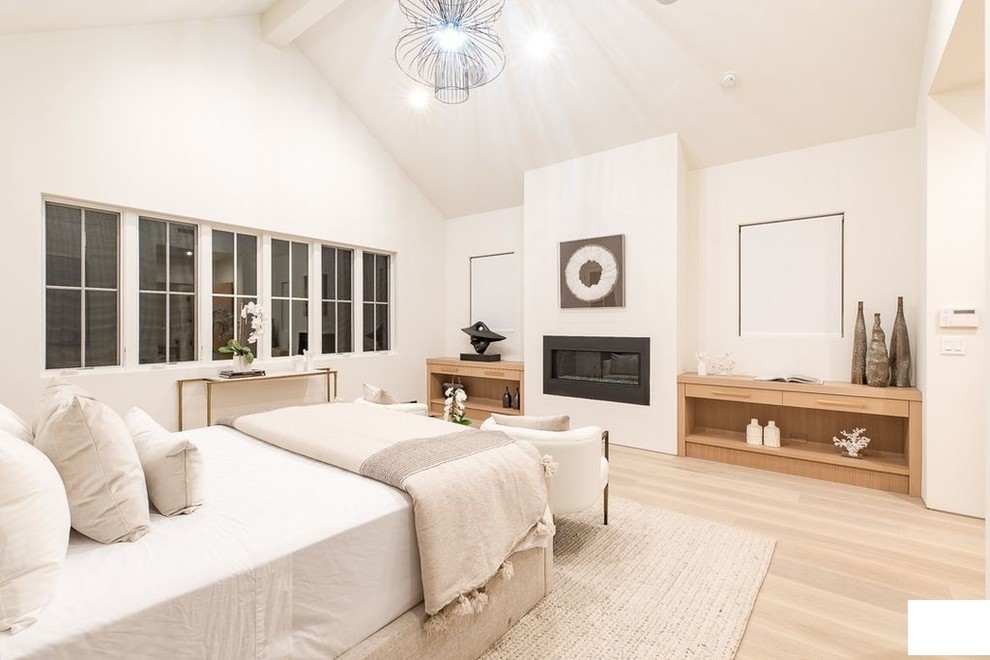 Inspiration for a large contemporary master bedroom in Los Angeles with white walls, light hardwood floors, a hanging fireplace, a wood fireplace surround and beige floor.