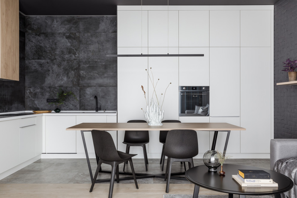 Photo of a contemporary open plan kitchen in Other with flat-panel cabinets, white cabinets, black splashback, no island, grey floor and white benchtop.
