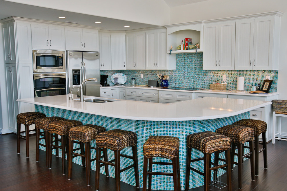 Photo of an expansive beach style l-shaped eat-in kitchen in Other with a double-bowl sink, shaker cabinets, white cabinets, blue splashback, mosaic tile splashback, stainless steel appliances, dark hardwood floors, with island, quartz benchtops and brown floor.