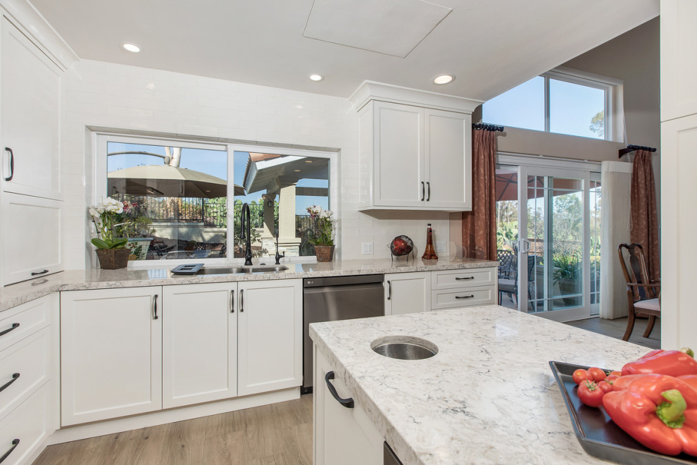 Photo of a small transitional u-shaped kitchen in San Diego with an undermount sink, shaker cabinets, white cabinets, quartz benchtops, white splashback, ceramic splashback, stainless steel appliances, porcelain floors, with island, beige floor and white benchtop.