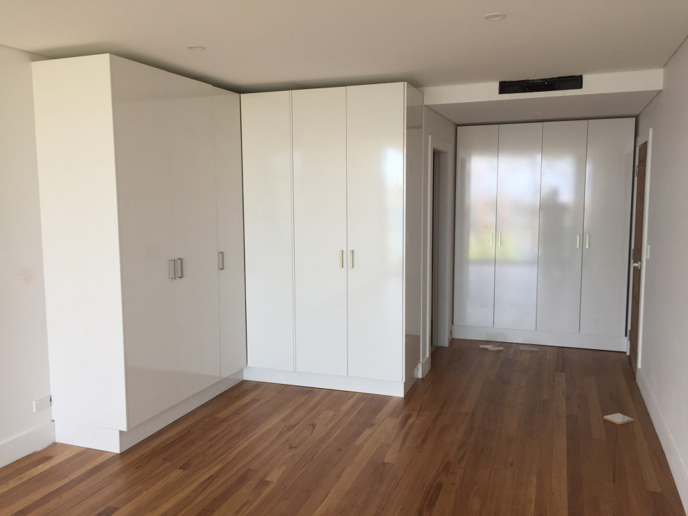 Large contemporary gender-neutral storage and wardrobe in Sydney with white cabinets, bamboo floors and brown floor.