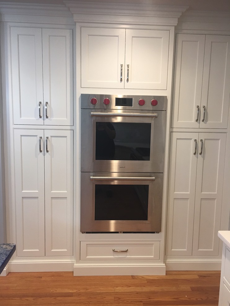 Kitchen - mid-sized transitional l-shaped medium tone wood floor and brown floor kitchen idea in Boston with a farmhouse sink, shaker cabinets, white cabinets, granite countertops, gray backsplash, subway tile backsplash, stainless steel appliances and an island