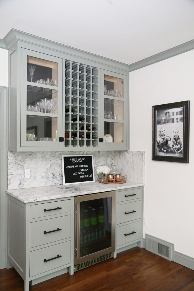 Photo of a small transitional single-wall wet bar in Other with glass-front cabinets, green cabinets, marble benchtops, grey splashback, marble splashback, medium hardwood floors, brown floor and grey benchtop.