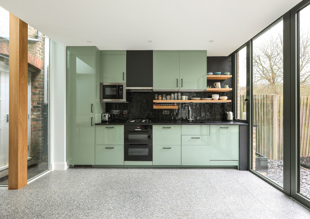 Inspiration for a mid-sized contemporary single-wall kitchen in London with a drop-in sink, flat-panel cabinets, green cabinets, solid surface benchtops, black splashback, ceramic splashback, stainless steel appliances, terrazzo floors, grey floor, black benchtop and no island.