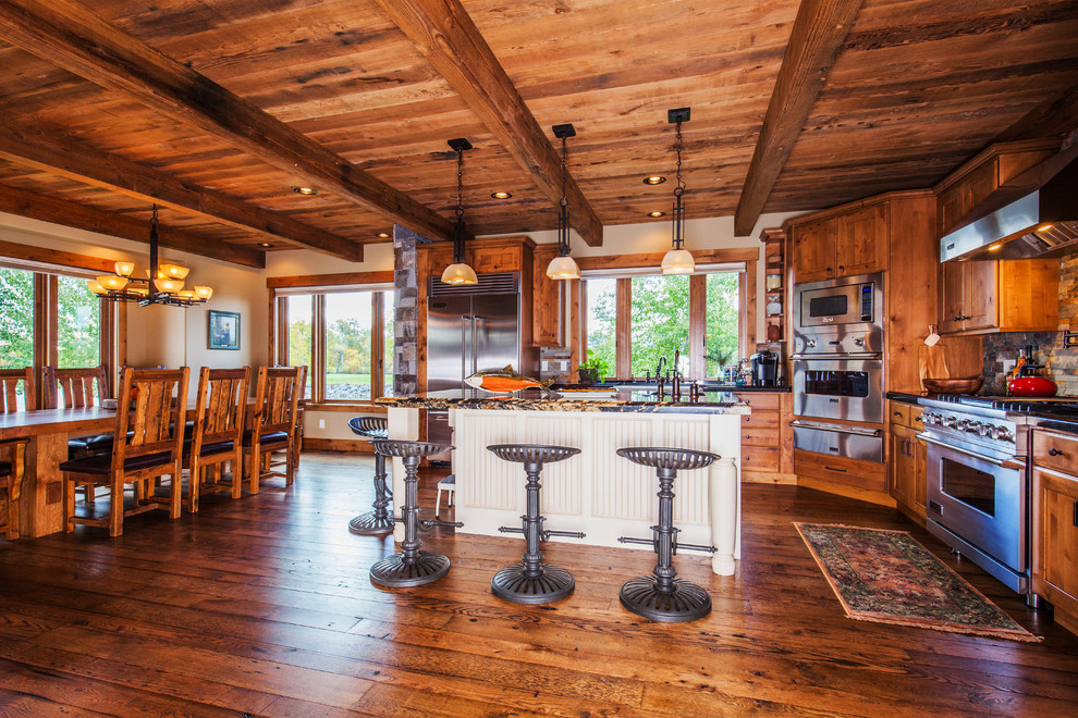 Mid-sized mountain style l-shaped dark wood floor open concept kitchen photo with a farmhouse sink, shaker cabinets, medium tone wood cabinets, granite countertops, multicolored backsplash, stone tile backsplash, stainless steel appliances and an island
