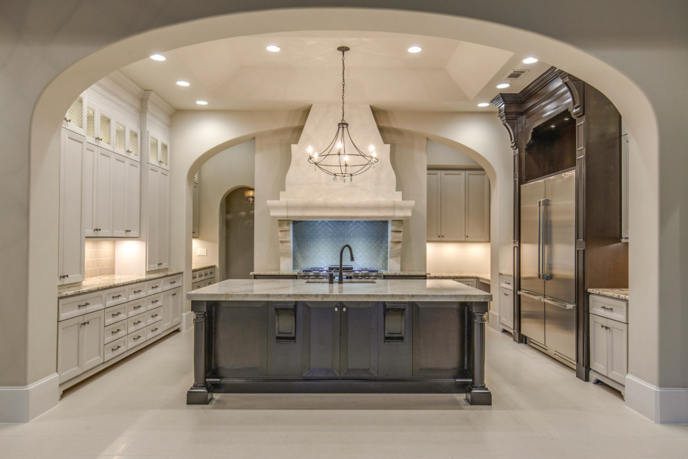 Inspiration for a large mediterranean u-shaped porcelain tile and beige floor kitchen remodel in Houston with an undermount sink, shaker cabinets, beige cabinets, granite countertops, beige backsplash, stainless steel appliances, an island, beige countertops and glass tile backsplash