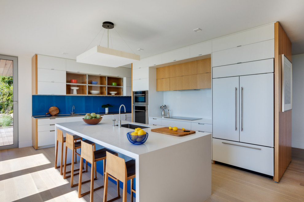 Design ideas for a large contemporary l-shaped open plan kitchen in Boston with an undermount sink, flat-panel cabinets, white cabinets, quartzite benchtops, blue splashback, glass sheet splashback, panelled appliances, light hardwood floors, with island, beige floor and white benchtop.