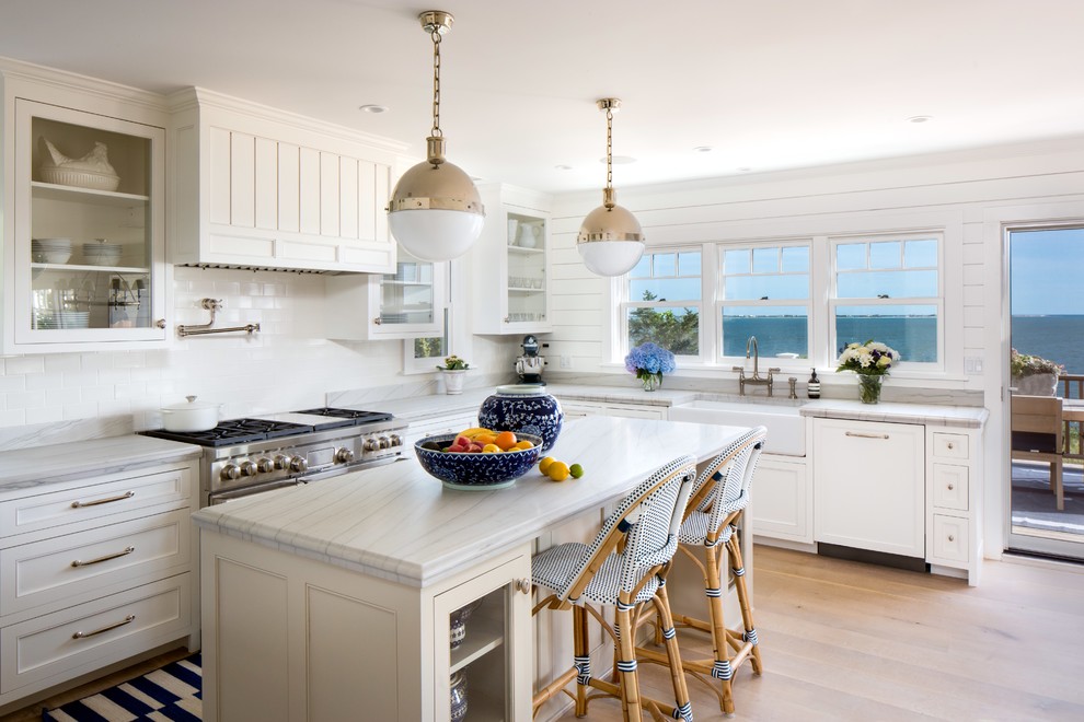 Large transitional u-shaped eat-in kitchen in New York with white cabinets, white splashback, white appliances, with island, a farmhouse sink, glass-front cabinets, marble benchtops and light hardwood floors.