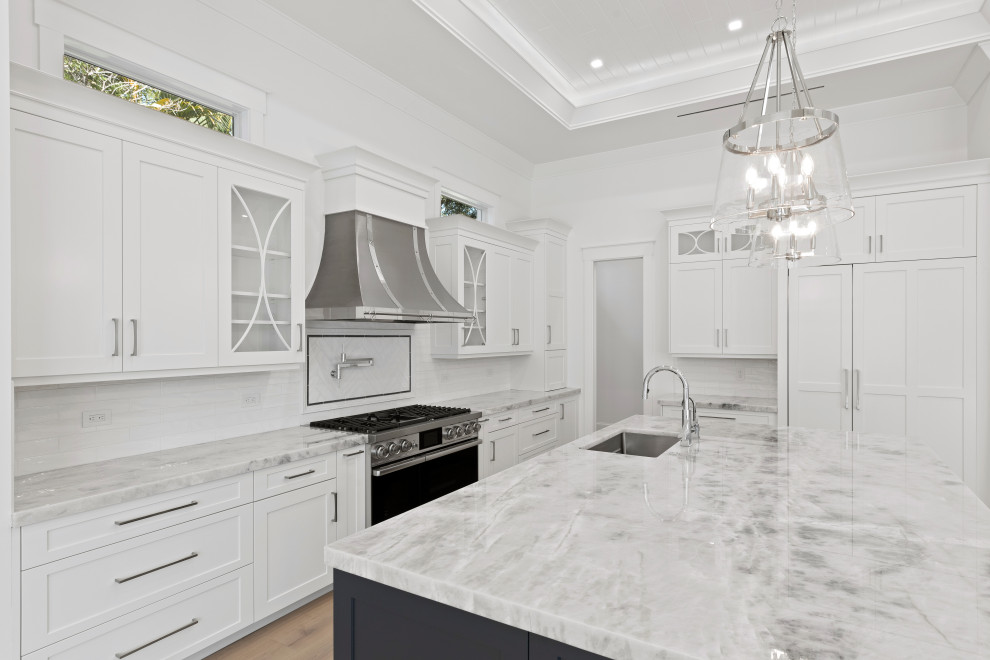 Inspiration for a large transitional l-shaped open plan kitchen in Miami with an undermount sink, shaker cabinets, white cabinets, marble benchtops, white splashback, ceramic splashback, panelled appliances, light hardwood floors, with island, beige floor and grey benchtop.