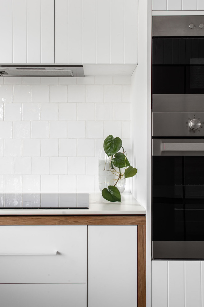 This is an example of a scandinavian l-shaped kitchen in Hobart with a farmhouse sink, white cabinets, white splashback, ceramic splashback, stainless steel appliances, no island and white benchtop.