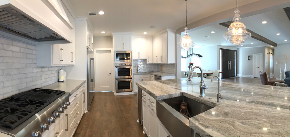 Example of a large transitional l-shaped medium tone wood floor and brown floor open concept kitchen design in Dallas with an undermount sink, shaker cabinets, white cabinets, quartz countertops, gray backsplash, ceramic backsplash, stainless steel appliances and an island